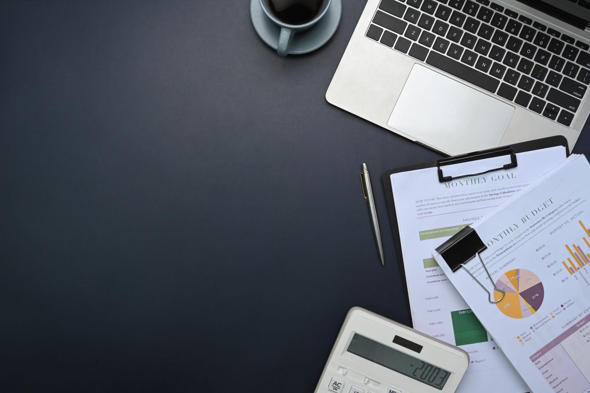 Top view of office desk with laptop, calculator, financial reports, and coffee cup on desk